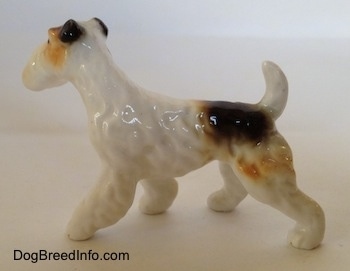 The left side of a white with black and tan bone china figurine of a Wire Fox Terrier. The figurine has hair details along its body.