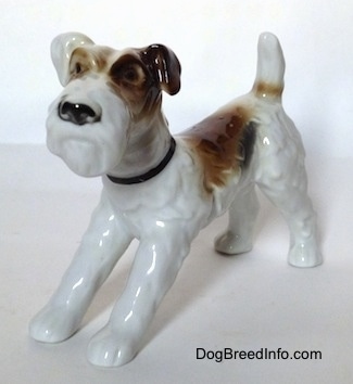 The front left side of a figurine of a white with black and brown Wire Fox Terrier. The figurine has black circles for eyes.
