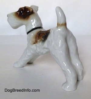 The back left side of a figurine of a white with black and brown Wire Fox Terrier. The figurine is glossy.
