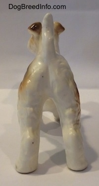 The back of a white with tan and black ceramic figurine of a Wire Fox Terrier. The figurine has its tail arched into the air.