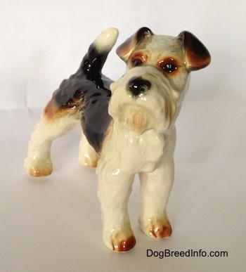 The front right side of a black and white with brown figurine of a Wire Fox Terrier. The figurine has black circles for eyes.