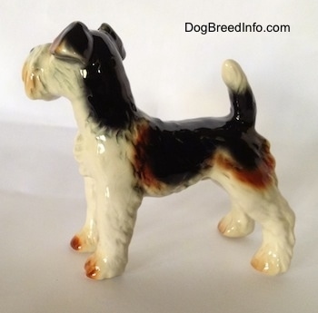 The left side of a figurine of a black and white with brown Wire Fox Terrier. The figurine has its tail arched in the air.