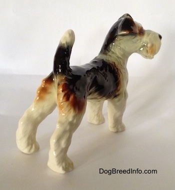The back right side of a black and white with brown Wire Fox Terrier figurine. The figurine has a long tail that is in the air.