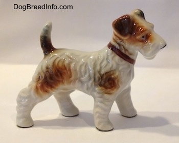 The right of a white with tan figurine of a porcelain Wire Fox Terrier standing. The figurine has a brown collar on.