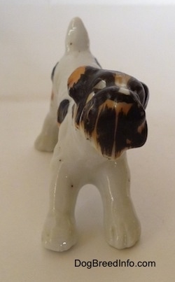 A white with black and brown bone china Wire Fox Terrier figurine in a play bow pose. The figurine has black circles for eyes.