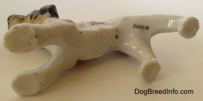 The underside of a Wire Fox Terrier figurine that is on its side. There is the black stamp of 'JAPAN' on its leg.
