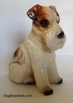The front right side of a white with black and brown ceramic Wire Fox Terrier sitting figurine. The figurine has black paws.