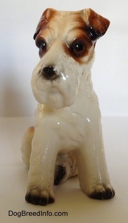 A ceramic figurine of a white with black and brown Wire Fox Terrier sitting. The figurine has a very detailed face.
