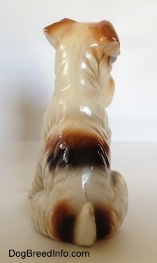 The back of a sitting white with black and brown ceramic Wire Fox Terrier figurine. The figurine has a brown and black spot above its short tail.