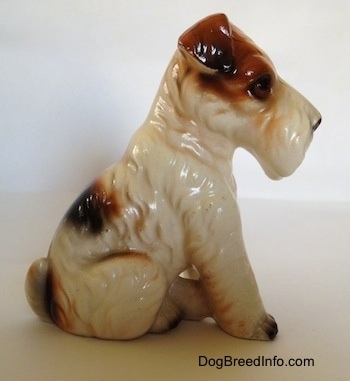 The right side of a ceramic white with black and brown Wire Fox Terrier in a sitting pose figurine. The figurine has fine hair details.