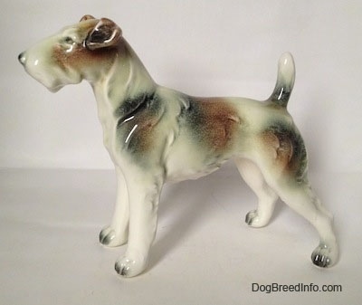 The left side of a white with brown and black Wire Fox Terrier figurine. The figurine has long legs with black tipped nails.