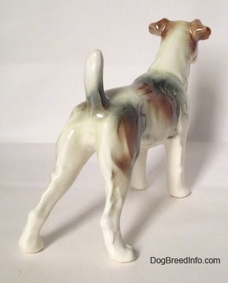 The back right side of a figurine of a white with brown and black Wire Fox Terrier. The figurine is glossy.
