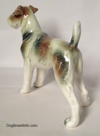 The back left side of a white with brown and black Wire Fox Terrier figurine. The figurine has brown and black patches along tis body.