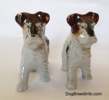 Two porcelain figurines of white with black and brown Wire Fox Terriers. They both have black dots for eyes.