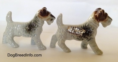 The right side of two white with black and brown Wire Fox Terrier figurines. The figurines have small legs.
