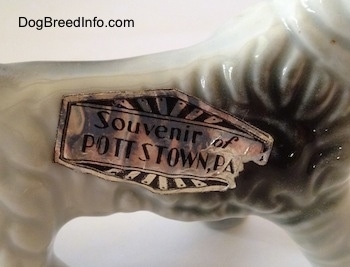 Close up - The underside of a porcelain Wire Fox Terrier figurine that has a sticker that reads 'Souvenir of Pottstown, PA'.