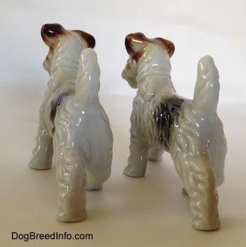 The back of two white with black and brown porcelain Wire Fox Terrier figurines. The figurines have fine hair details.