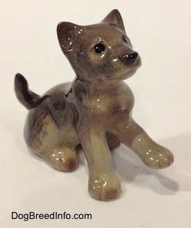 The front right side of a figurine of a Wolf cub sitting. The figurine is glossy.