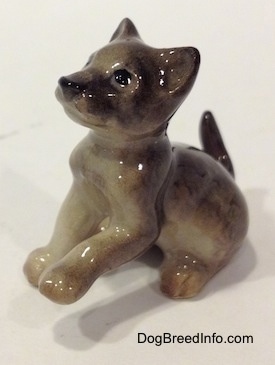 The left side of a gray figurine of a Wolf cub sitting. The figurines left paw is in the air.