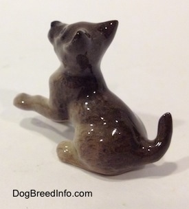The back left side of a figurine of a Wolf cub sitting. The tail of the figurine is arched in the air.