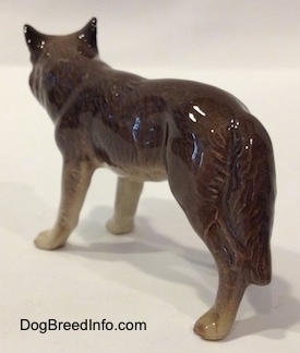 The back left side of a brown with tan figurine of a Wolf. The figurine has long tail that hang next to its leg.