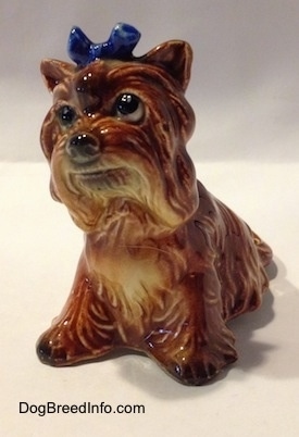 The front left side of a brown with tan Yorkshire Terrier sitting figurine. The figurine has a blue bow in its hair.