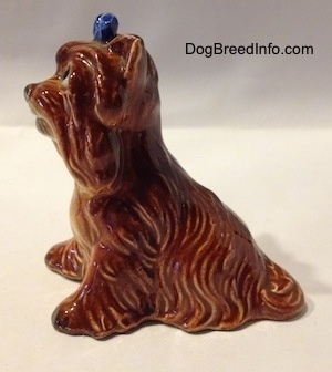 The left side of a brown with tan figurine of a sitting Yorkshire Terrier. The figurine has fine hair brushings along tis side.