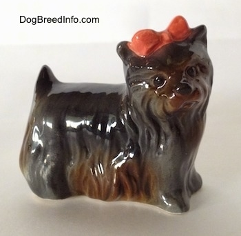 The right side of a gray with brown figurine of a Yorkshire Terrier that has a red bow in its hair.