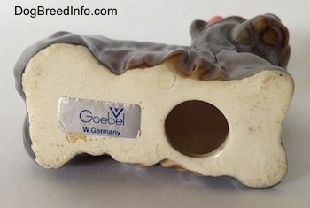 The underside of a gray with brown figurine of a Yorkshire Terrier. There is a huge hole on the underside and to the left of it is the sticker of Goebel W.Germany.