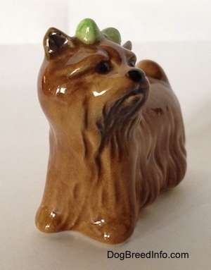 The front left side of a brown figurine of a Yorkshire Terrier figurine. The figurine has a black nose and small black circles for eyes.