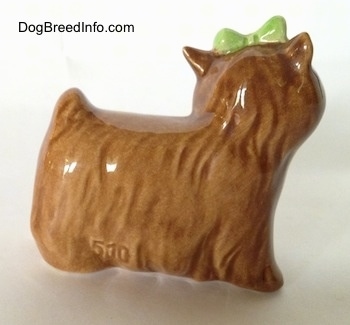 The right side of a brown Yorkshire Terrier figurine with a green bow in its hair. Its ears are small and sticking in the air.