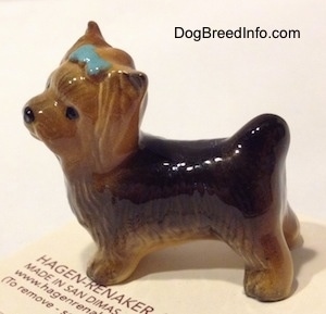 The left side of a black with brown Yorkshire Terrier figurine with a bluw bow in its hair. The figurine is glossy.
