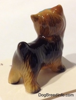The back right side of a black with brown figurine of a Yorkshire Terrier. The figurine has its short ears in the air.