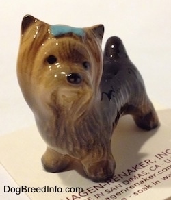The front right side of a figurine of a black with brown Yorkshire Terrier with a blue bow in its hair. The figurine has black circles for eyes.