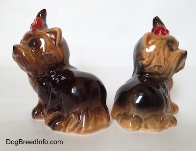 The back side of two black with brown figurines of sitting Yorkshire Terriers. The figurines have short ears.