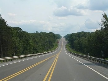 A long highway with a yellow stripe down the center and trees on each side.